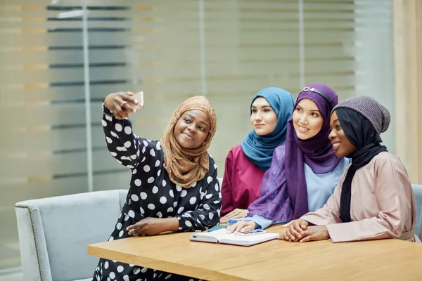 Four Muslim student girls taking selfie in college classroom sitting together — Stock Photo, Image