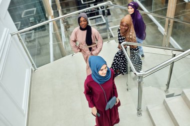 Alışveriş merkezinin merdivenlerinde yürüyen dört Müslüman kız grubu.