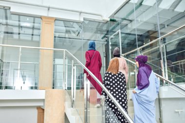 Alışveriş merkezinin merdivenlerinde yürüyen dört Müslüman kız grubu.