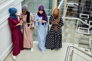 Müslüman çok ırklı kızlar Afrikalı bir kadının elindeki akıllı telefona bakıyorlar.