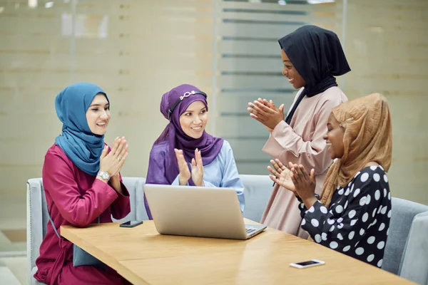 Muslim asian and african women in head scarfs and hijab using laptop in cafe
