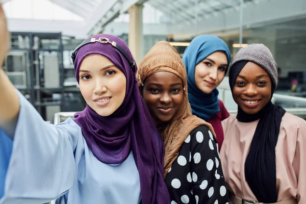 Group of four multiethnic Muslim women in traditional hijab take selfie in mall