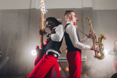 Gösterişli iki müzisyen dumanlı sahnede gösteri yapıyor.