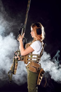 Asker kadın ince belinde tabak taşıyıcı taşıyor, elinde keskin nişancı tüfeği var.