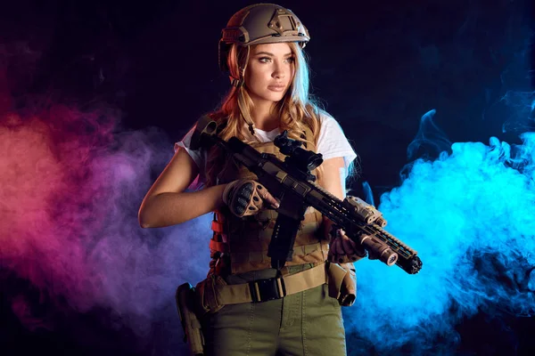 Linda mujer francotiradora con rifle en las manos de pie en traje militar en la oscuridad — Foto de Stock