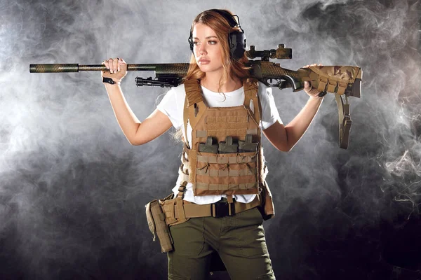 Mulher franco-atirador bonito com rifle nas mãos em pé em roupa militar na escuridão — Fotografia de Stock