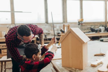 Baba ve oğlu ahşap bir atölyede birlikte çalışıp kuş evi inşa ediyorlar.