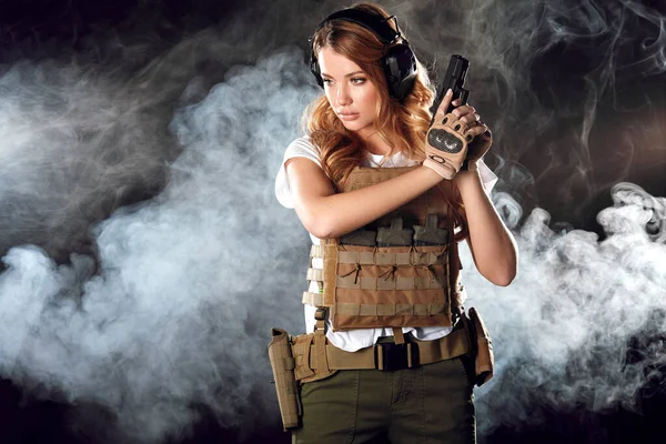 Mujer rubia armada dispara con pistola a un objetivo en la oscuridad con nubes de humo — Foto de Stock