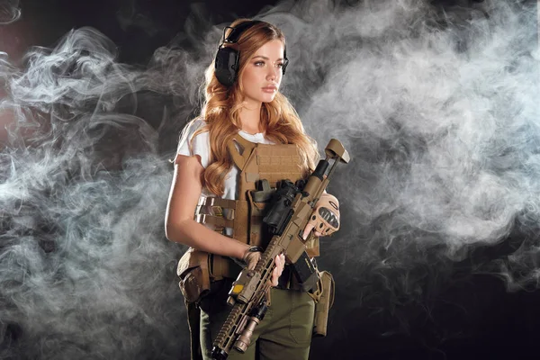 Fegyveres női katona katonai álcázó egyenruhában, fejhallgatóval védve. — Stock Fotó