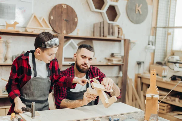 Baba ve oğlu ahşap bir atölyede birlikte çalışıp kuş evi inşa ediyorlar.
