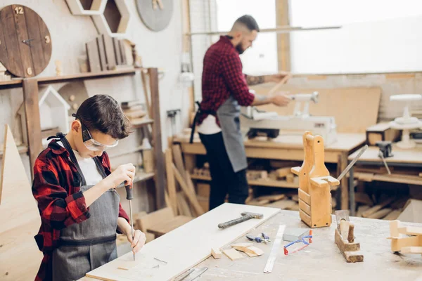 Father and little son at wooden workshop using screwdriver.