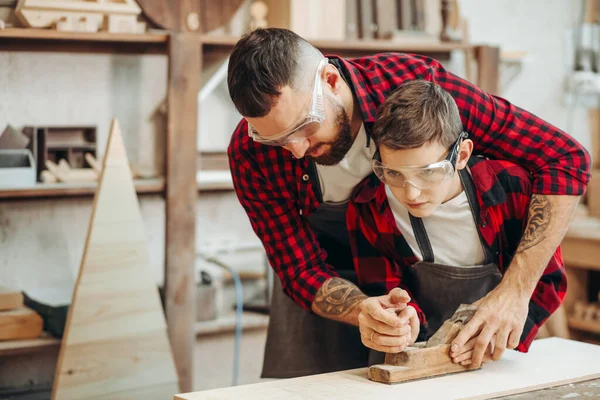 Kaukasische mannelijke timmerman omhelst zijn zoon om vliegtuig te gebruiken tijdens het werken met hout — Stockfoto