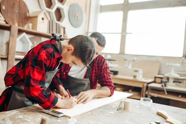 Little boy helps his carpenter father measuring the wooden plank in workshop. — Stock Photo, Image