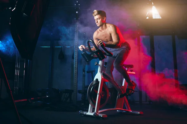 Cardio Workout. Shirtless man training on bicycle, cycling mashine in gym — Stock Photo, Image