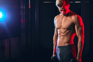 Kas gövdesi olan erkek antrenör, spor salonunda elinde dambıllar tutuyor.