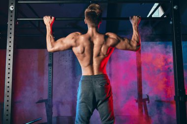 Spor salonunda beden eğitimi alan genç bir vücut geliştirici. Koyu renk spor salonunda geniş tutuş egzersizi yapıyor..