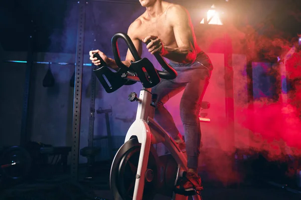 Сильний білий спортсмен без сорочки тренування в симуляторі велосипеда в спортзалі . — стокове фото