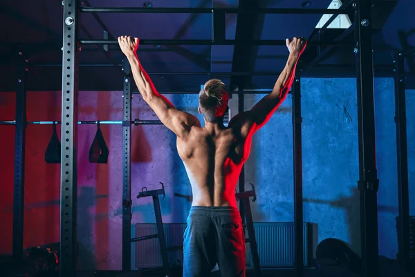 Jonge bodybuilder training in donkere sportschool. Terug - Breed-Grip Front Pull-Up — Stockfoto