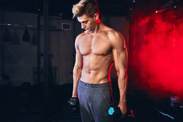 Hombre atlético de fitness bombeando músculos con mancuernas en el gimnasio interior — Foto de Stock