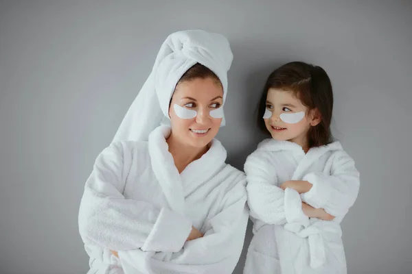 Retrato de una agradable madre joven en albornoz y su hija pequeña en parches para los ojos —  Fotos de Stock