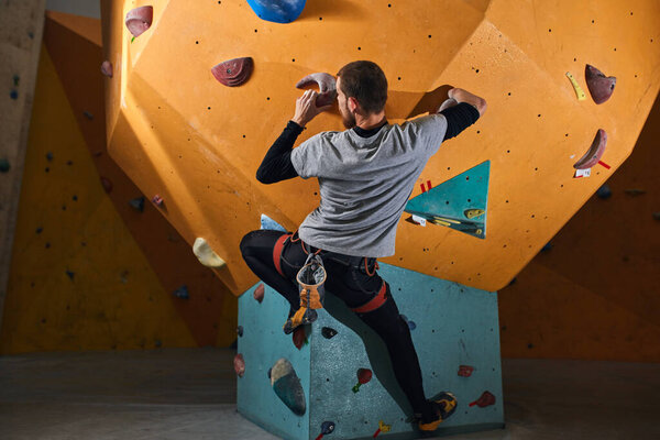 Rear view of powerful physically challenged boulderer climbing at rock wall