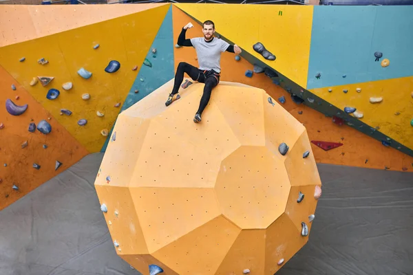 Fröhlicher, körperlich behinderter Boulderer sitzt auf einer großen künstlichen Felswand — Stockfoto