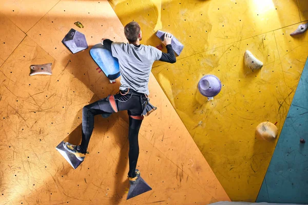 Pemandangan belakang olahragawan tanpa lengan bawah memanjat dinding batu kuning di dalam ruangan — Stok Foto