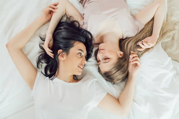 Vrouwen met eerlijk en donker haar spinding tijd op het bed, — Stockfoto