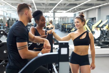 Spor salonunda antrenörle konuşan iki farklı atletik kadın.