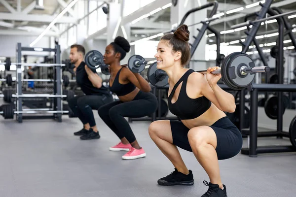 Sportieve mensen, multi-etnische groep uit te voeren oefeningen met zware gewichten in de sportschool — Stockfoto