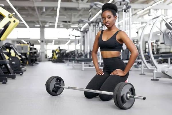 crossfit african woman sitting at gym, resting after cross-fit workout with barbell