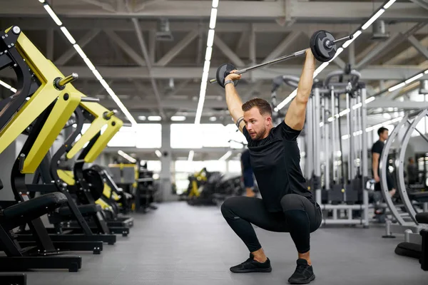 Sportler hockt im Fitnessstudio und hebt eine große Langhantel — Stockfoto