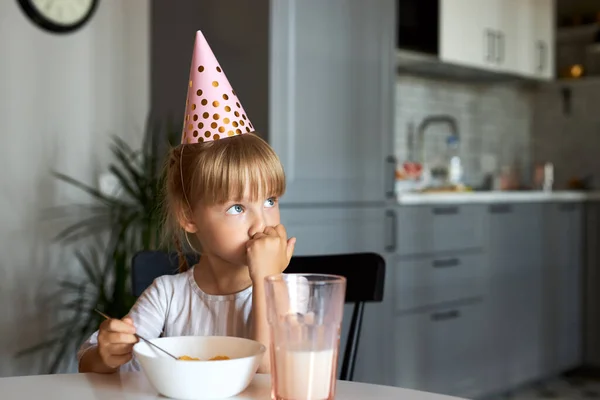 Malé dítě dívka sedět se snídaní na sobě párty klobouk — Stock fotografie