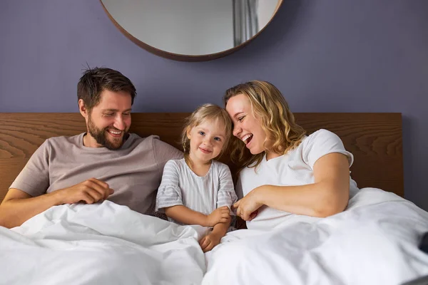 Mutlu bir aile ve çocuklu bir kız sabah yatakta yatarken gülüyor. — Stok fotoğraf