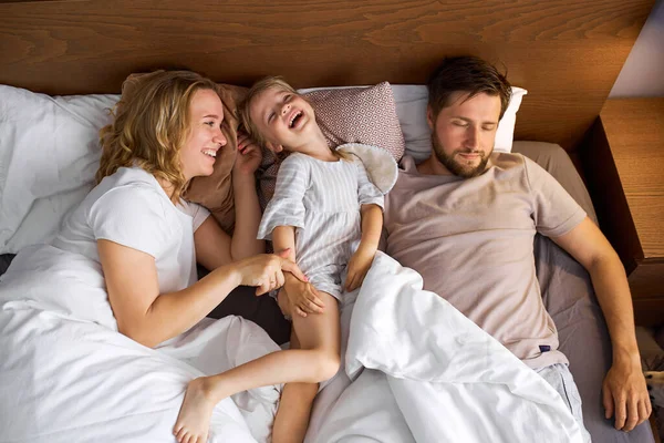 Mutter und Tochter haben Spaß im Bett, während der Vater schläft — Stockfoto