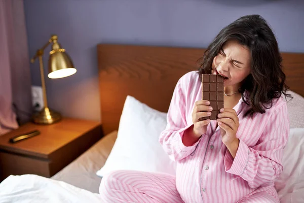 Pregnant woman takes a bite of milk chocolate — Stock Photo, Image