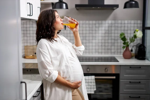 Вид збоку на вагітну жінку, яка п'є апельсиновий сік вдома — стокове фото