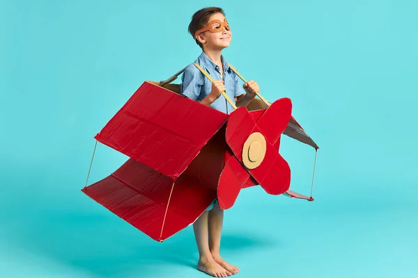 Молодий кавказький пілот хлопчика літає картонна коробка ізольована на синьому фоні — стокове фото