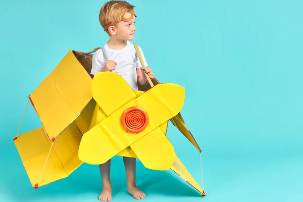 Kid boy playing with yellow cardboard airplane isolated on blue