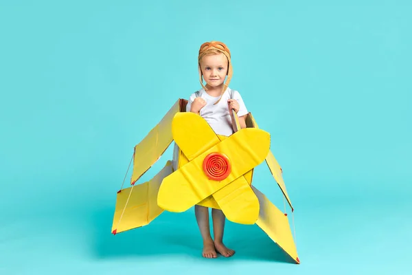 Хороший маленький хлопчик у жовтій іграшковій площині стоїть ізольовано в синьому — стокове фото