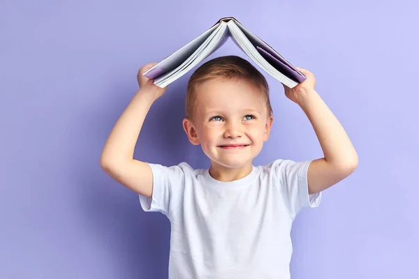 Улыбающийся мальчик с книгой над головой — стоковое фото
