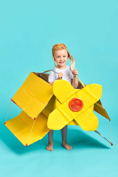 Nice small boy wearing yellow toy plane stand isolated in blue Royalty Free Stock Photos