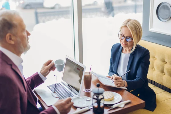 Encantadora mujer rubia y anciano desayunando y discutiendo un plan de negocios — Foto de Stock