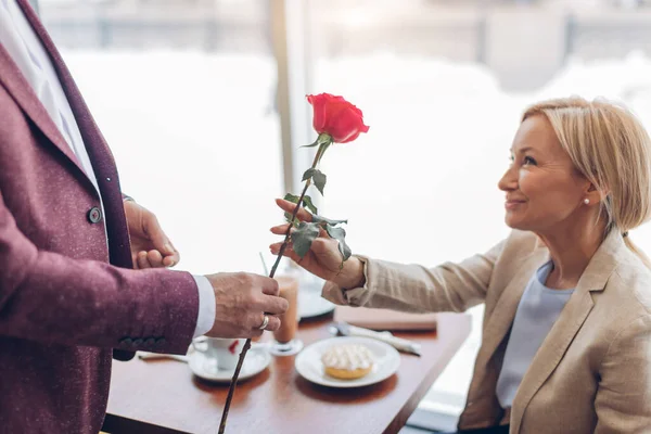 Homem elegante dando uma bela rosa para sorrir bela mulher loira no café — Fotografia de Stock