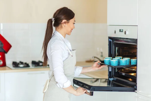 Glad attraktiv awesome flicka sätta bakplåt med muffins i ugnen — Stockfoto