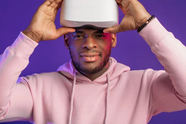 Afrikaanse man draagt virtual reality bril geïsoleerd op donker paarse achtergrond — Stockfoto