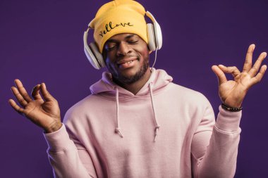 Kapüşonlu ve kulaklıklı Afrikalı bir adam, mutlu bir ifade. Müzik, millet.