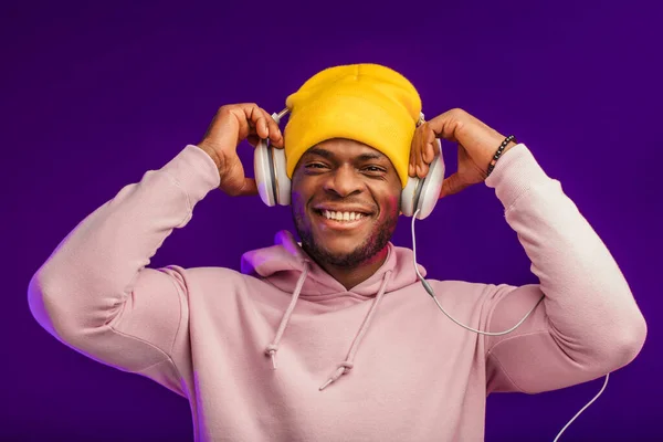 Afrikaanse man in hoodie met hoofdtelefoon geïsoleerd, gelukkige uitdrukking. Muziek, mensen. — Stockfoto
