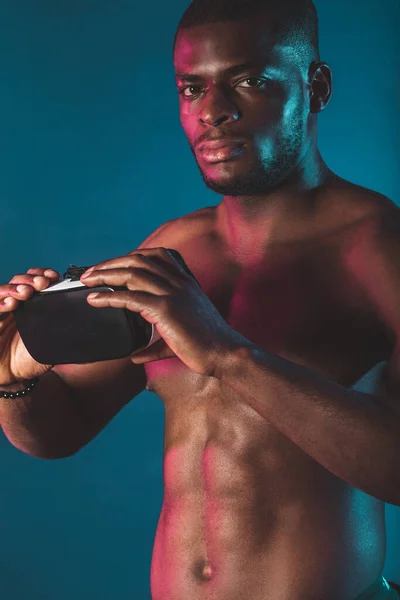 Joven deportista africano con cuerpo musculoso sosteniendo auriculares VR en azul, de cerca. —  Fotos de Stock