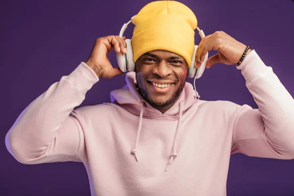 Afrikaanse man in hoodie met hoofdtelefoon geïsoleerd, gelukkige uitdrukking. Muziek, mensen. — Stockfoto